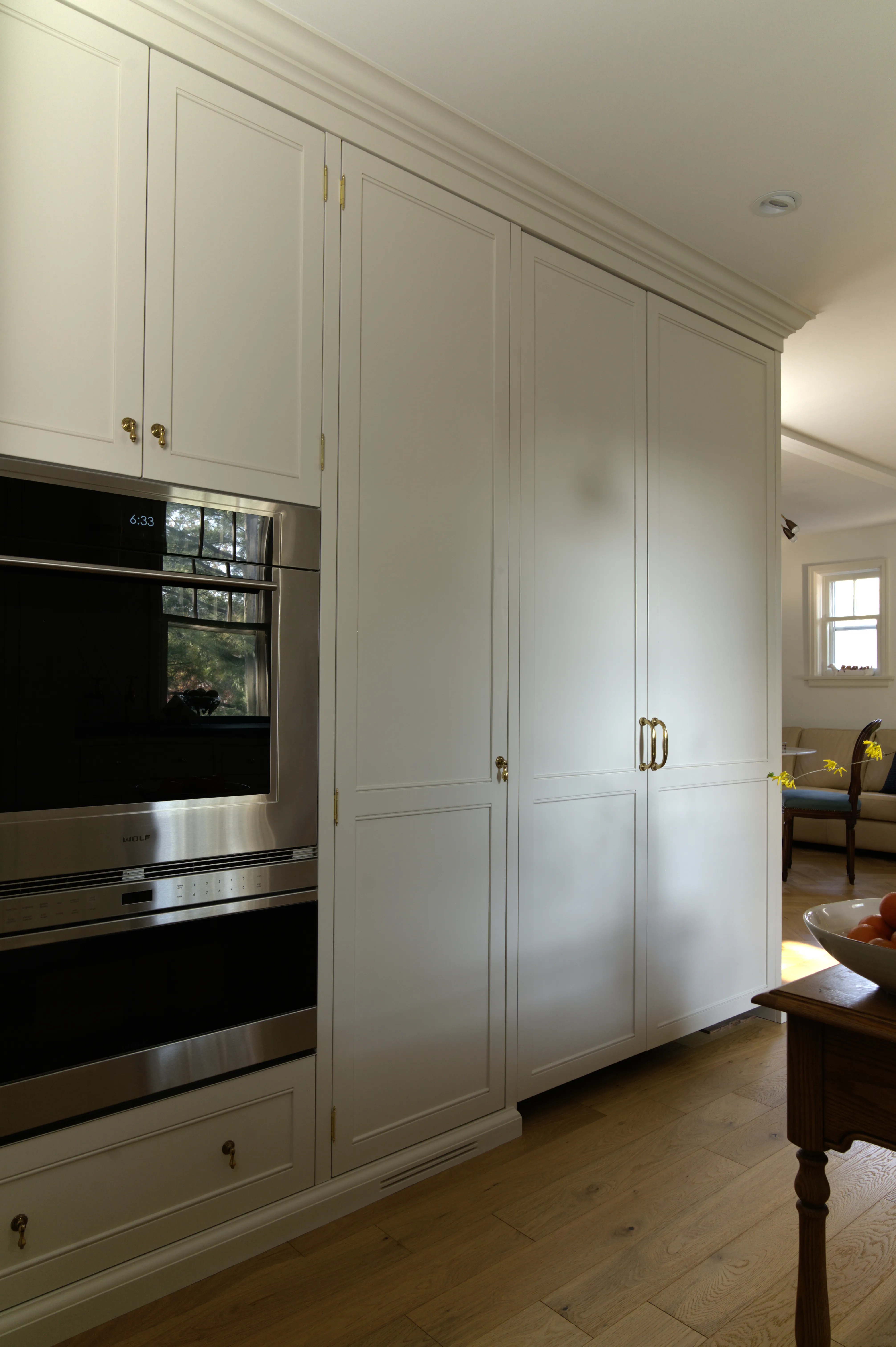 Custom floor-to-ceiling pantry cabinetry with integrated Wolf M Series wall oven and warming drawer, finished in cream with unlacquered brass hardware, designed by Nathallie Isabel in a 1940s home in Aurora.